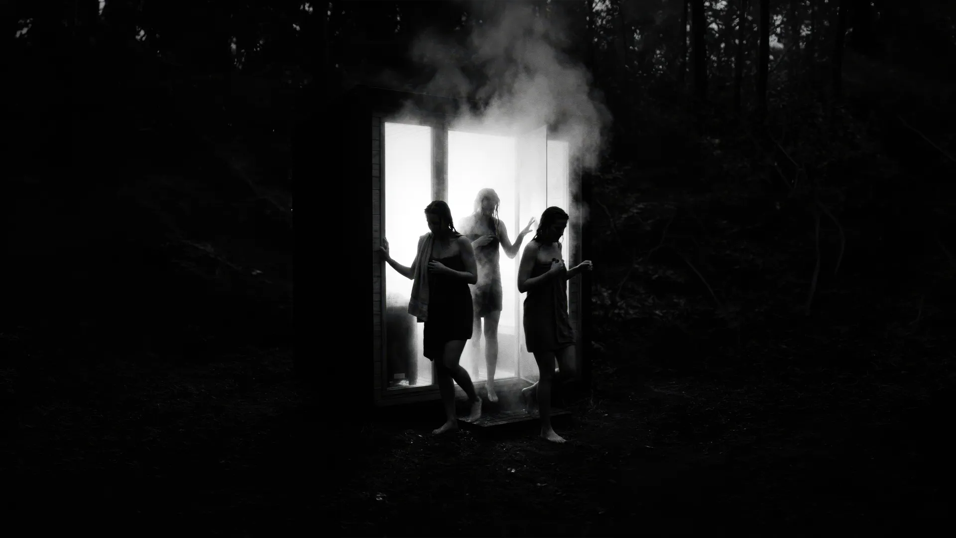 Trois personnes dans la vapeur, à la porte d’un sauna Ørigin, la nuit en forêt